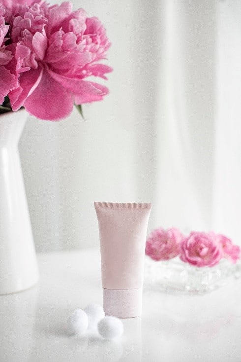 Photo montrant un packaging de produit cosmétique rose pâle à côté d'un bouquet de fleur