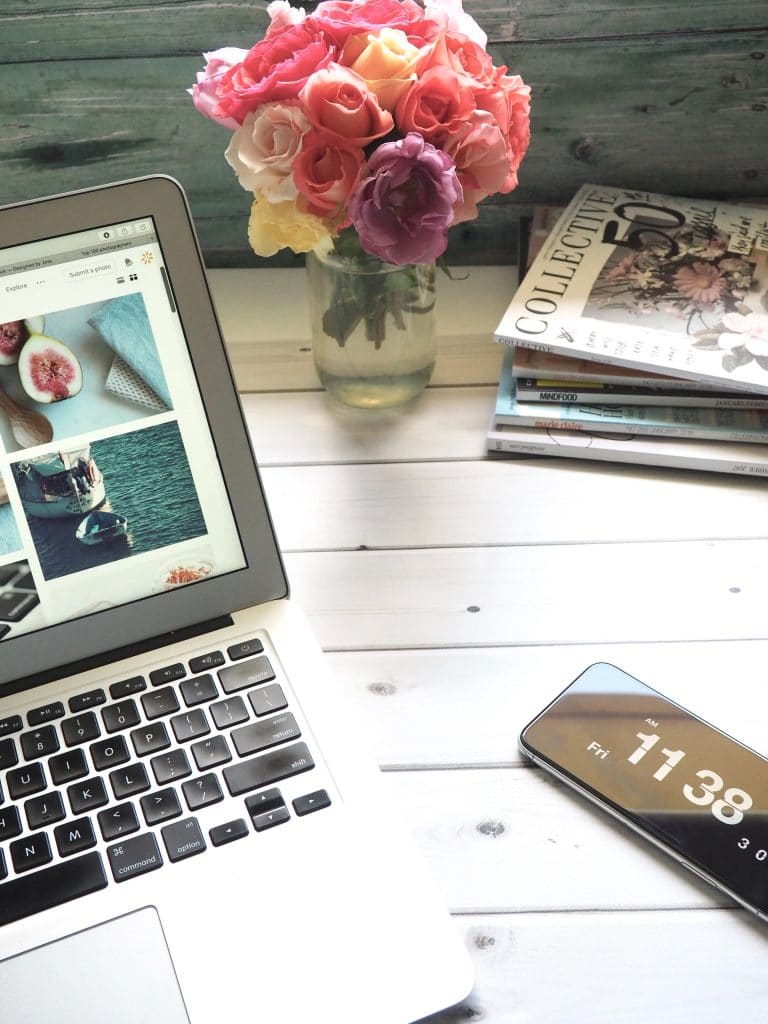 Ordinateur posé sur une table avec un bouquet de fleurs et des magazines